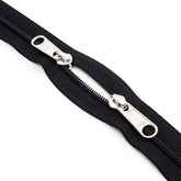 Cremallera doble YKK negra con tiradores plateados, dientes y tela visibles sobre fondo blanco. DUBBEL-RITS-150-YKK