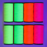 Eight spools of neon sewing thread in bright green, orange, and pink on a purple background. GOLDMANN-SET-FLUOR