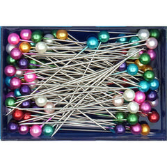 Close-up van Prym parel kopspelden (SKU PRYM-028625) met diverse gekleurde koppen (roze, groen, goud, blauw, paars, wit, rood) in een transparant plastic doosje. | PRYM-028625