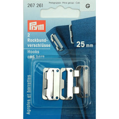 Prym rok- en broekhaken 25mm zilverkleurig in originele verpakking, met de tekst '2 Rockbund-verschluesse Hooks and bars 25 mm'. De haken zijn deels zichtbaar op een blauwe stof. SKU PRYM-267261. | PRYM-267261