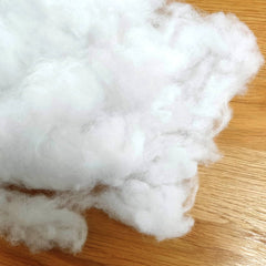 Plukje witte polyester vulling voor knuffels en hobby, los op houten ondergrond. 8719214301010 1000KG