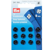 Prym black 9mm snap fasteners, 12 pieces on card packaging, showing loose items and attached to fabric. PRYM34164 4002273411640