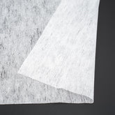 Wit vlieseline materiaal, textuur en dikte zichtbaar, op donkere achtergrond. PLAKVLIES-STND-90X200