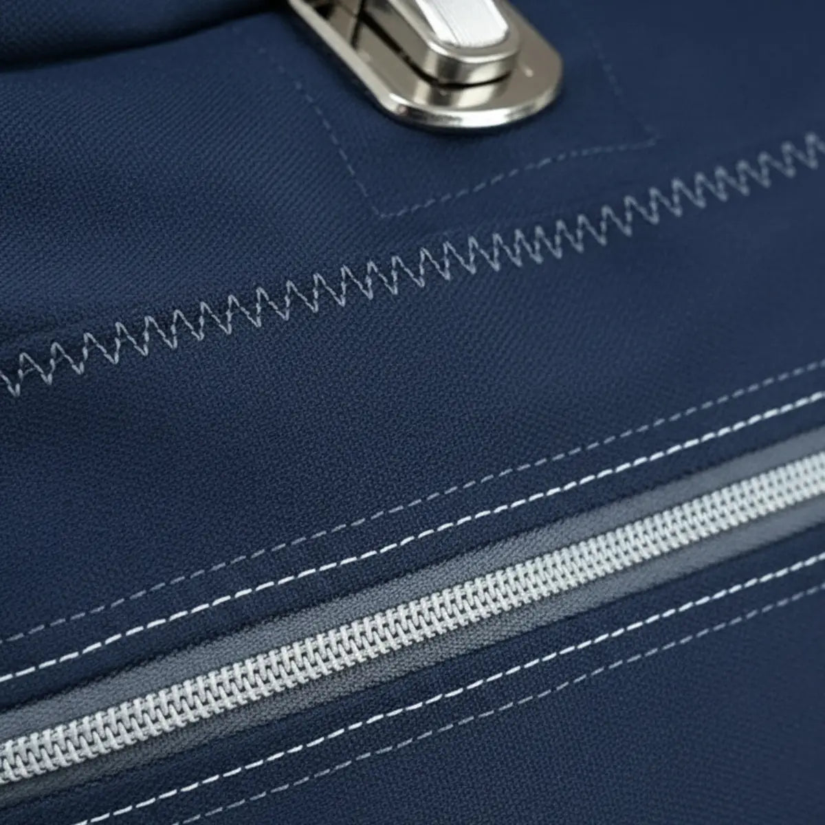 Close-up van donkerblauwe stof met witte stiksels, een rits en een metalen sluiting, demonstrerend de sterkte van Gutermann naaigaren. GUTERMANN-STERK-SET-734528 | GUTERMANN-STERK-SET-734528