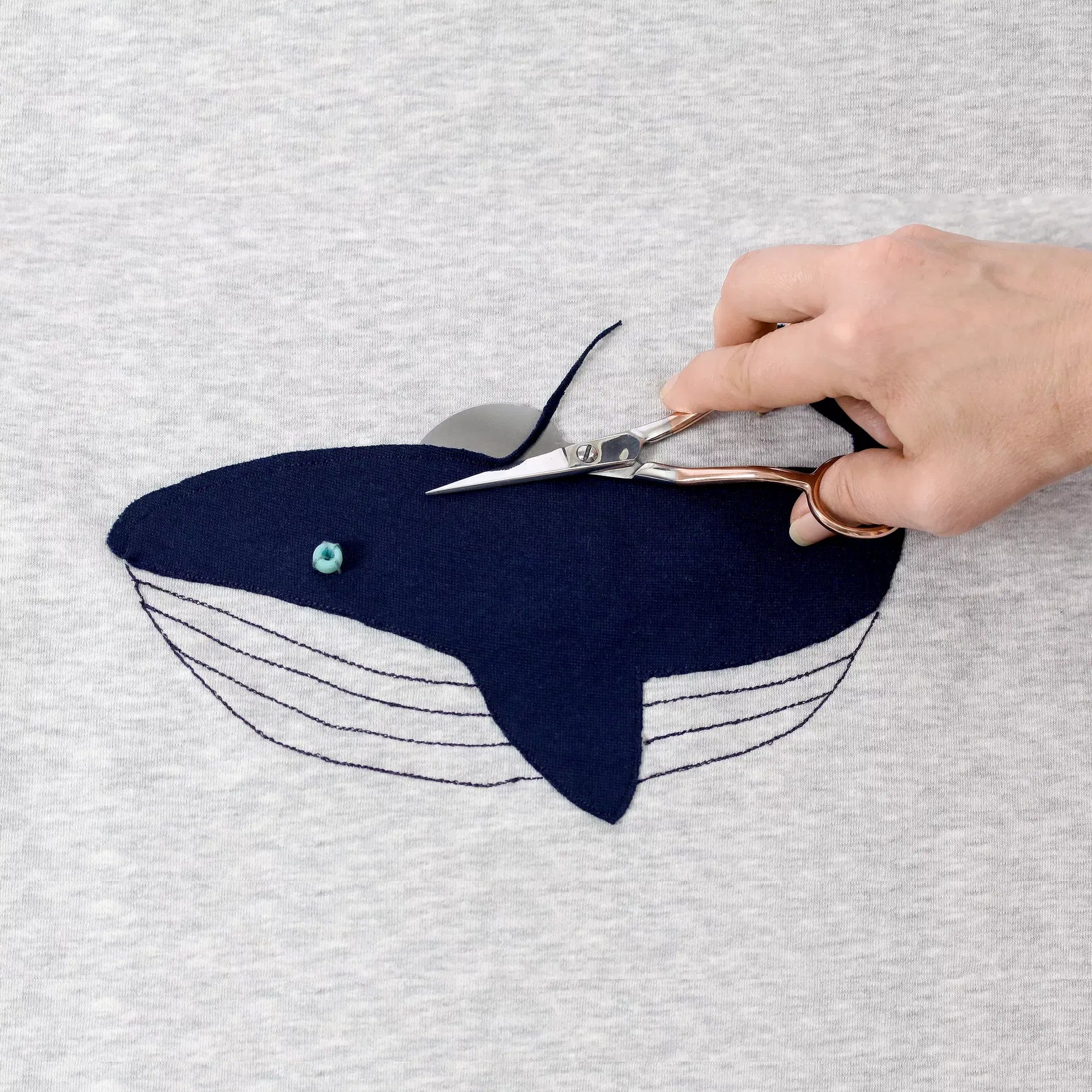Prym applicatieschaar trimt een donkerblauwe walvis applicatie op een grijs T-shirt | PRYM-610570 | 4002276105706